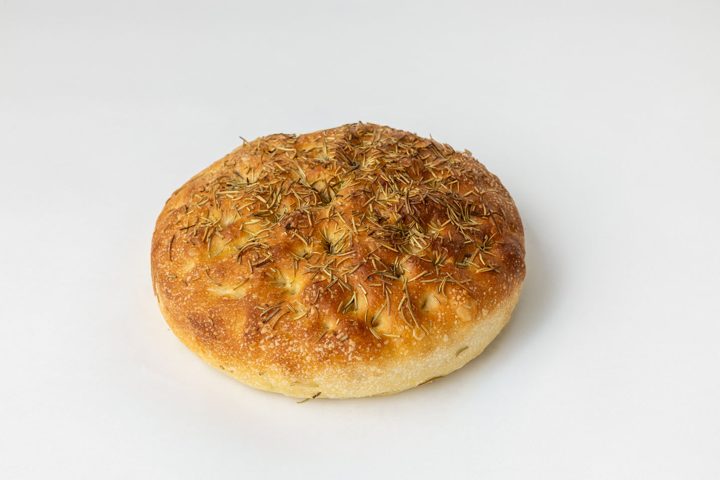 Round loaf of bread with a golden-brown crust and dried rosemary on a white background
