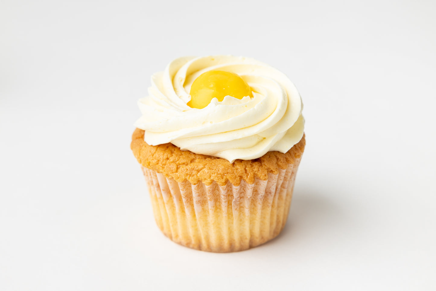 Cupcake with white frosting and a lemon on top against a white background