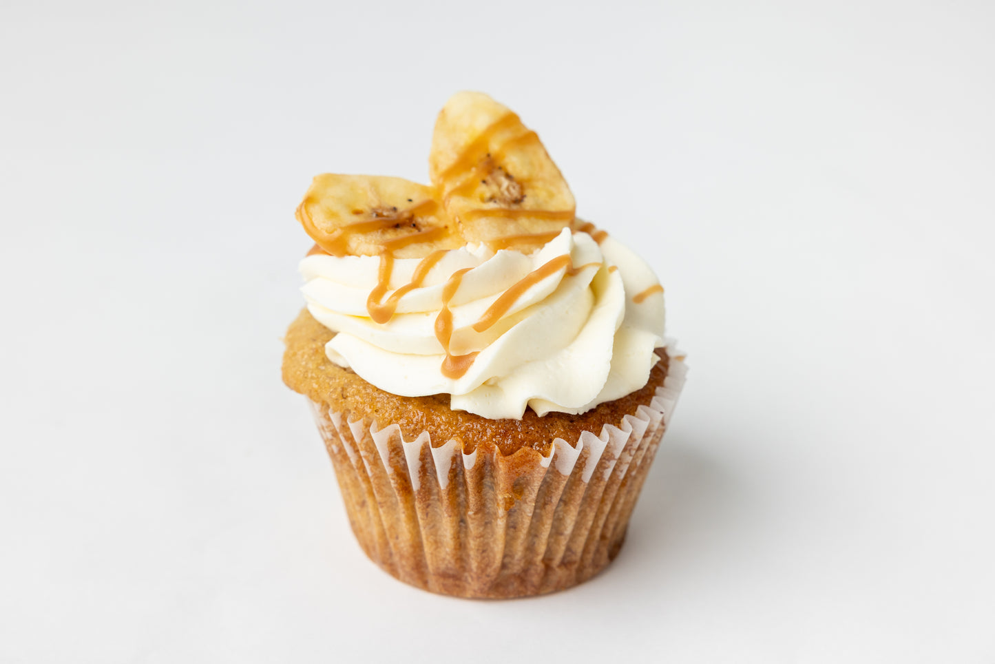 Banana cupcake with white frosting, banana chips and caramel drizzle on a white background