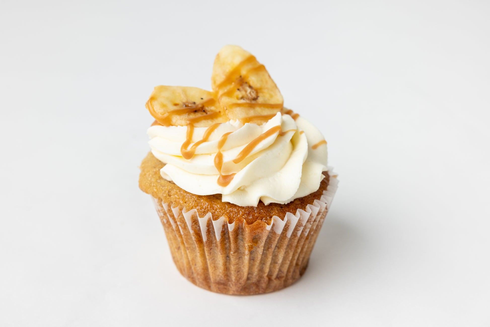 Banana cupcake with white frosting, banana chips and caramel drizzle on a white background