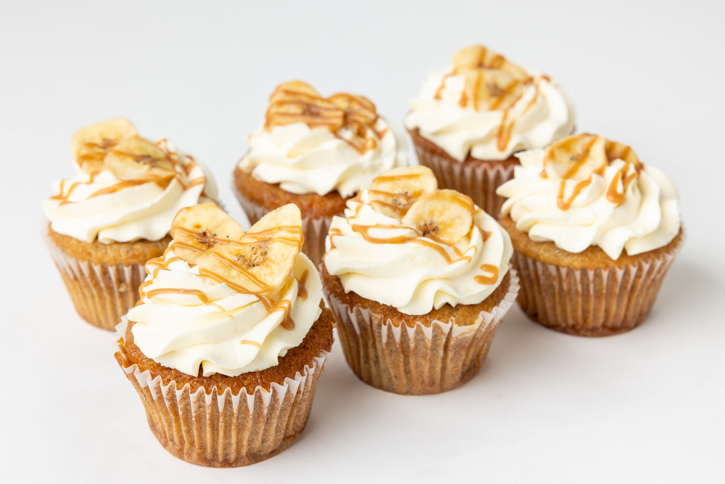 Banana cupcakes with cream cheese frosting and caramel drizzle on a white background