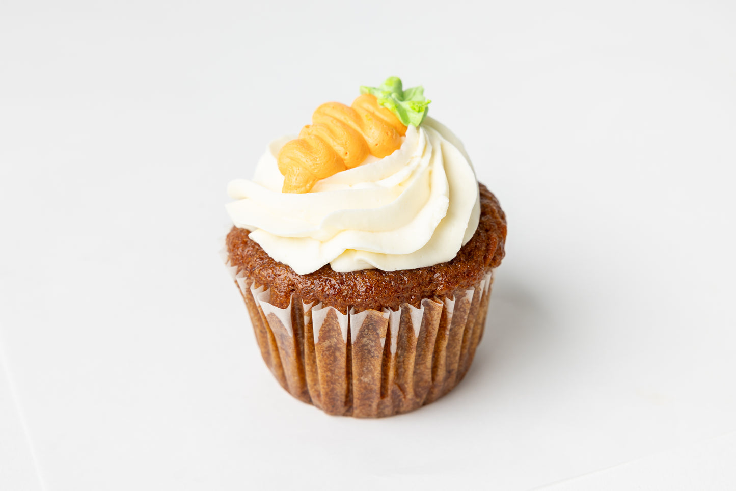 Carrot cake cupcake with cream cheese frosting and a decorative carrot on a white background