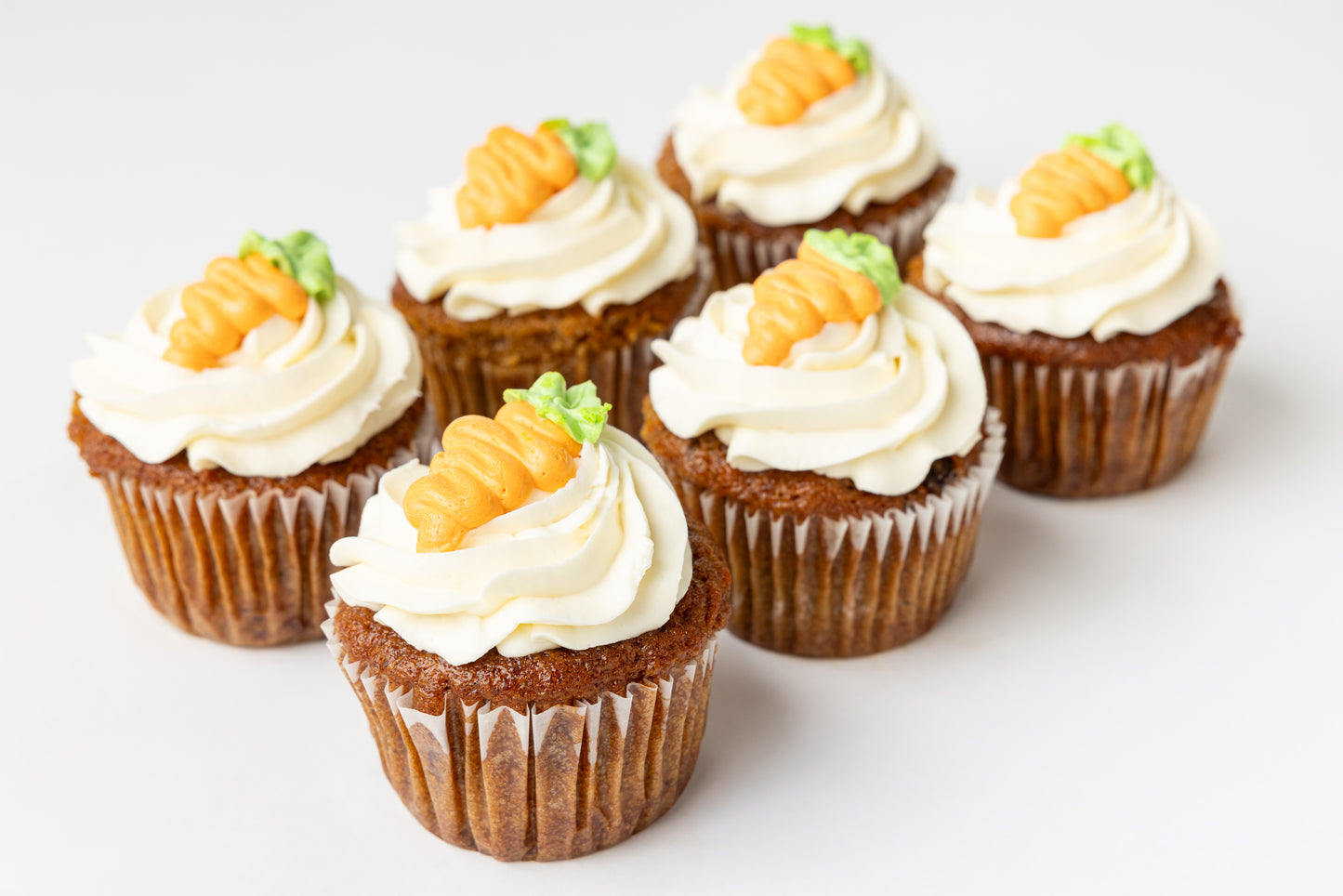 Carrot cupcakes with cream cheese frosting and small carrot decorations on a light background