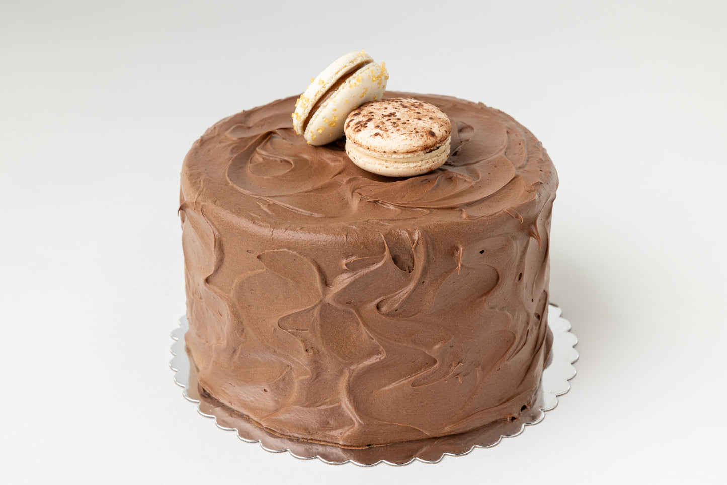 Chocolate frosted cake with two macarons on a white background