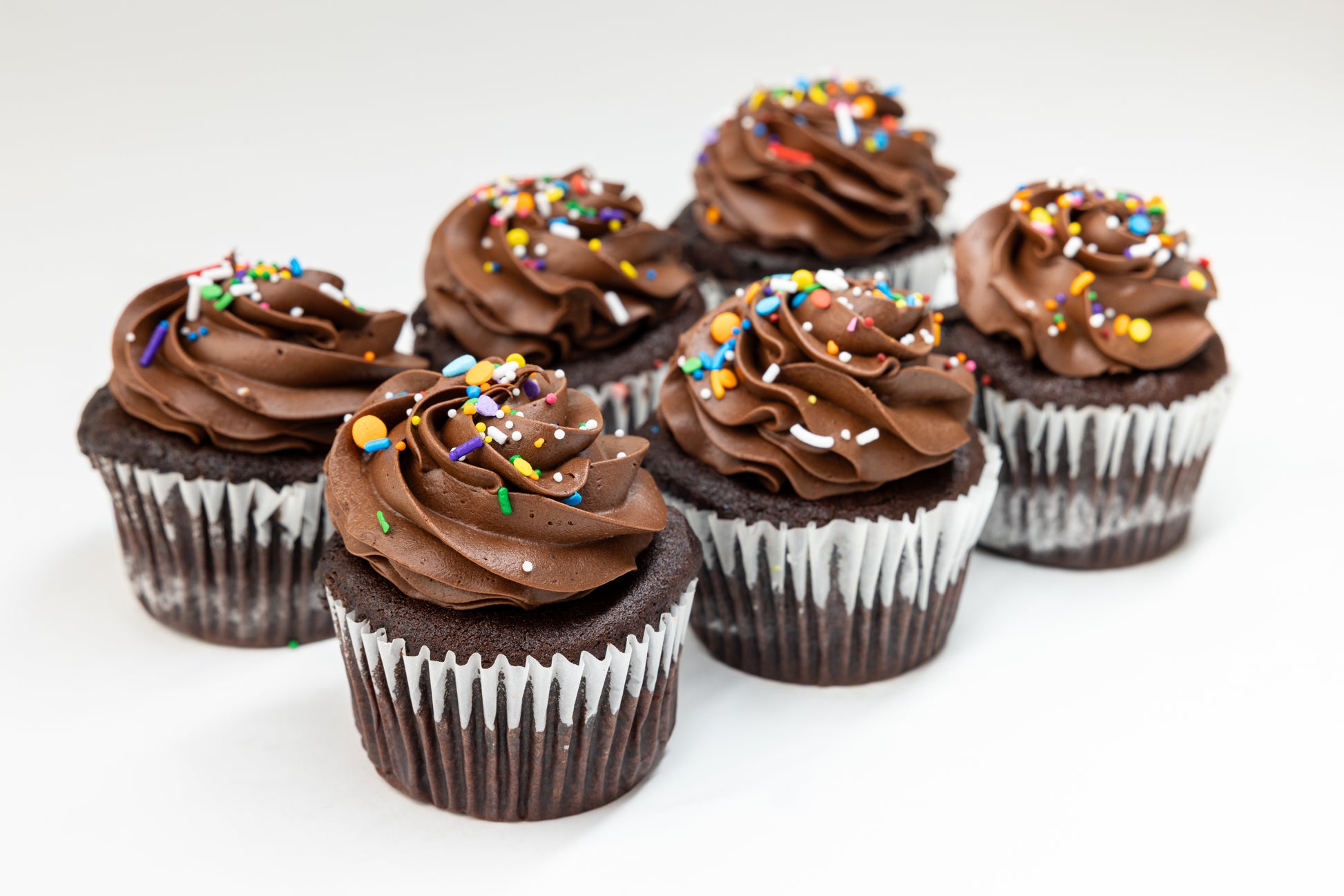 Chocolate cupcakes with colourful adn chocolate frosting and sprinkles on a white background