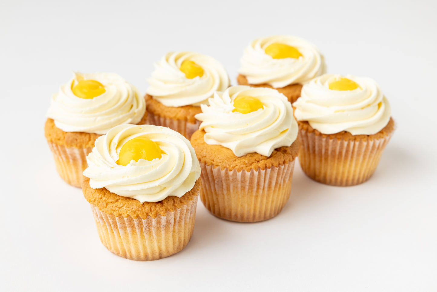 Six vanilla cupcakes with buttercream frosting and lemon centers on a white background
