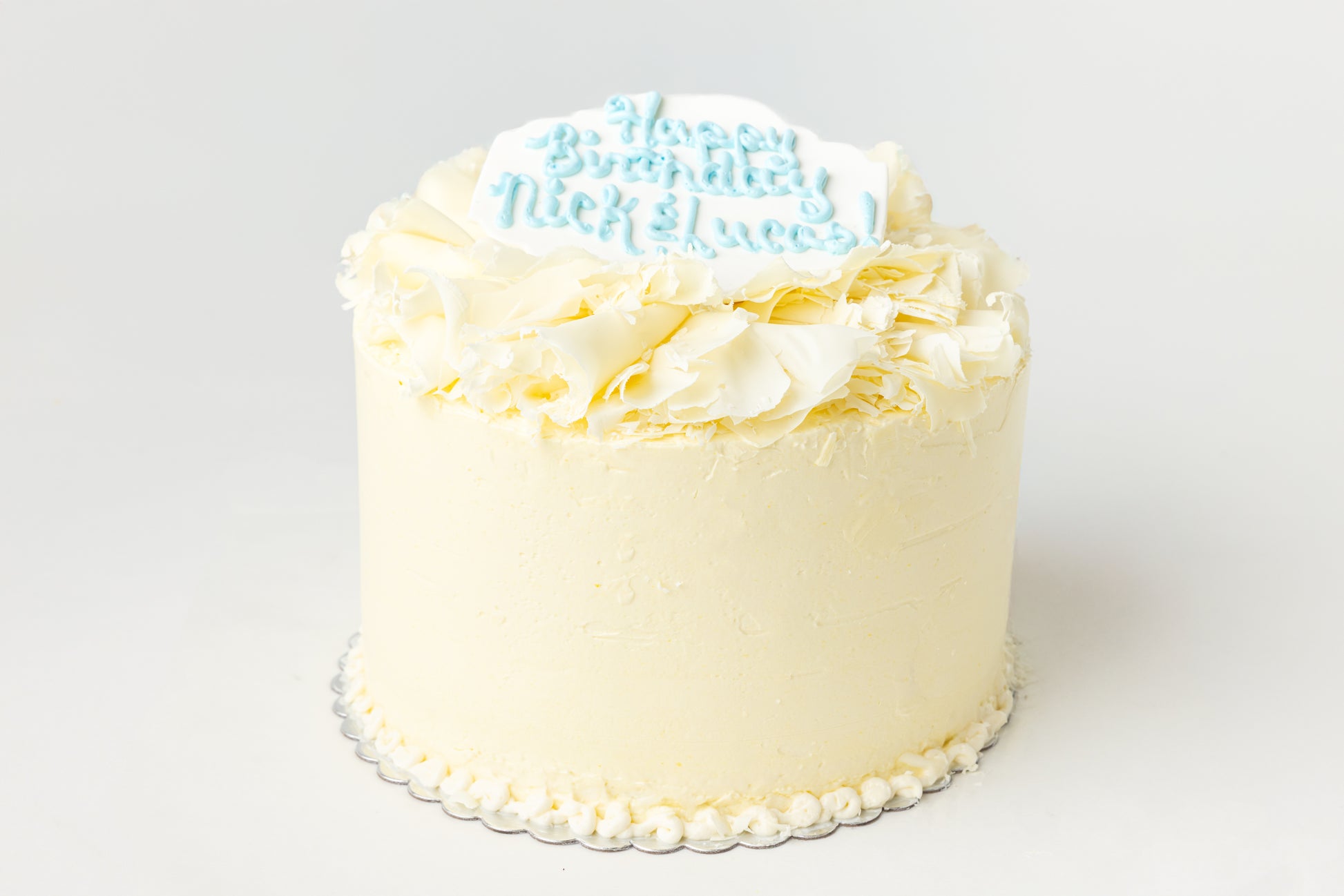 White cake with white chocolate curls and a plaque with writing elements on a white background