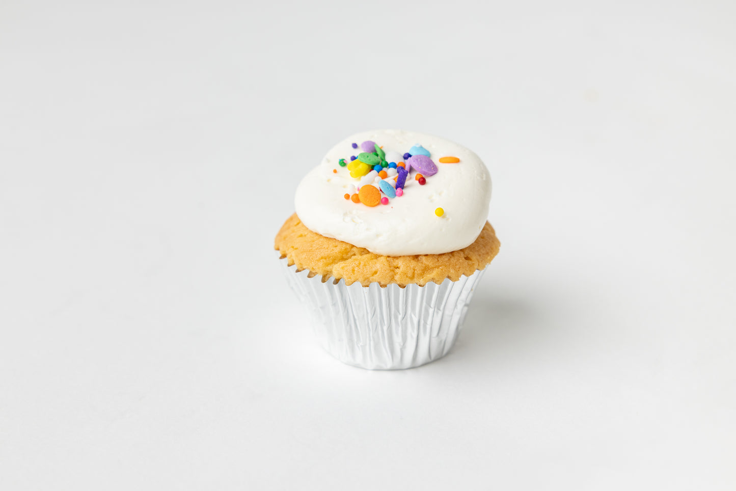 Cupcake with white frosting and colorful sprinkles on a light gray background