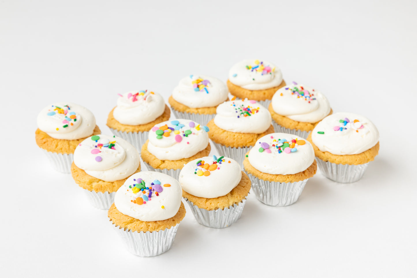 Row of vanilla cupcakes with white frosting and colorful sprinkles on a light background