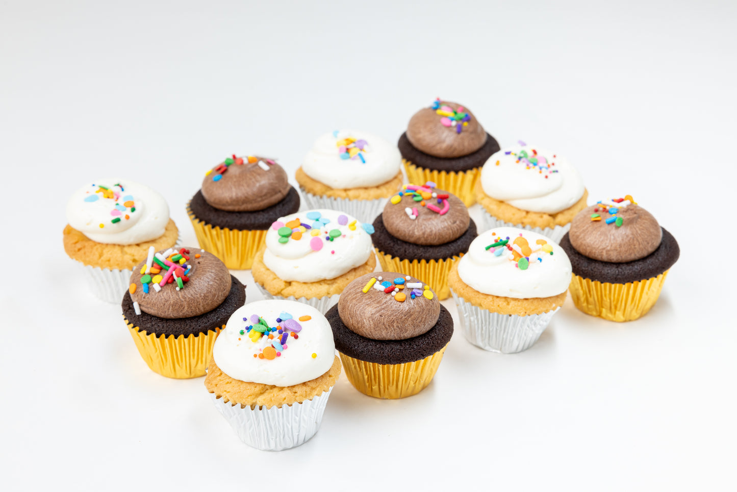 Assorted vanilla and chocolate cupcakes with different frostings and sprinkles on a white background