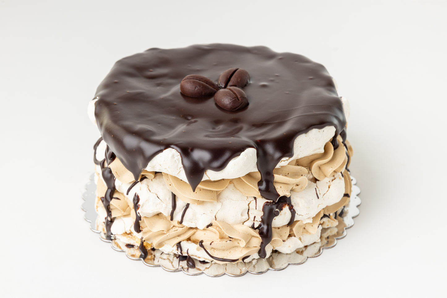 Layered meringue cake with chocolate ganache, coffee buttercream and coffee beans on a white background