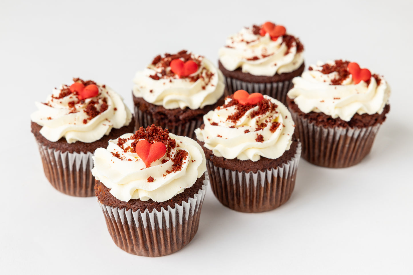 red velvet cupcakes with cream cheese frosting and red heart decorations on a light background
