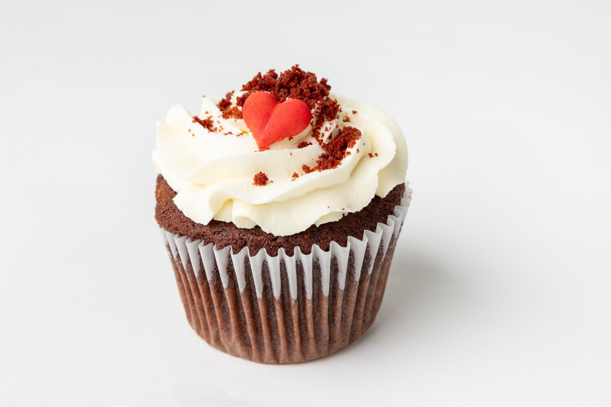 Red velvet cupcake with white cream cheese frosting and a red heart on a white background