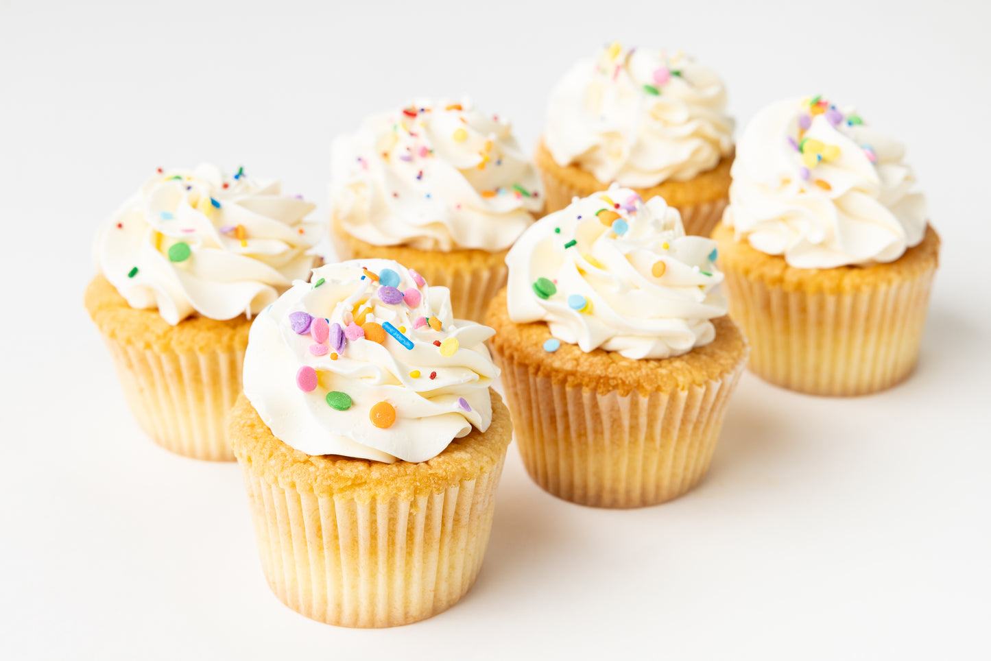 Cupcakes with vanilla buttercream frosting and colorful sprinkles on a white background